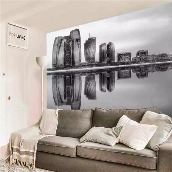 Ein gemütliches Wohnzimmer mit einer grauen Couch und einer großflächigen Wanddekoration, die eine Skyline und deren Spiegelung im Wasser zeigt.