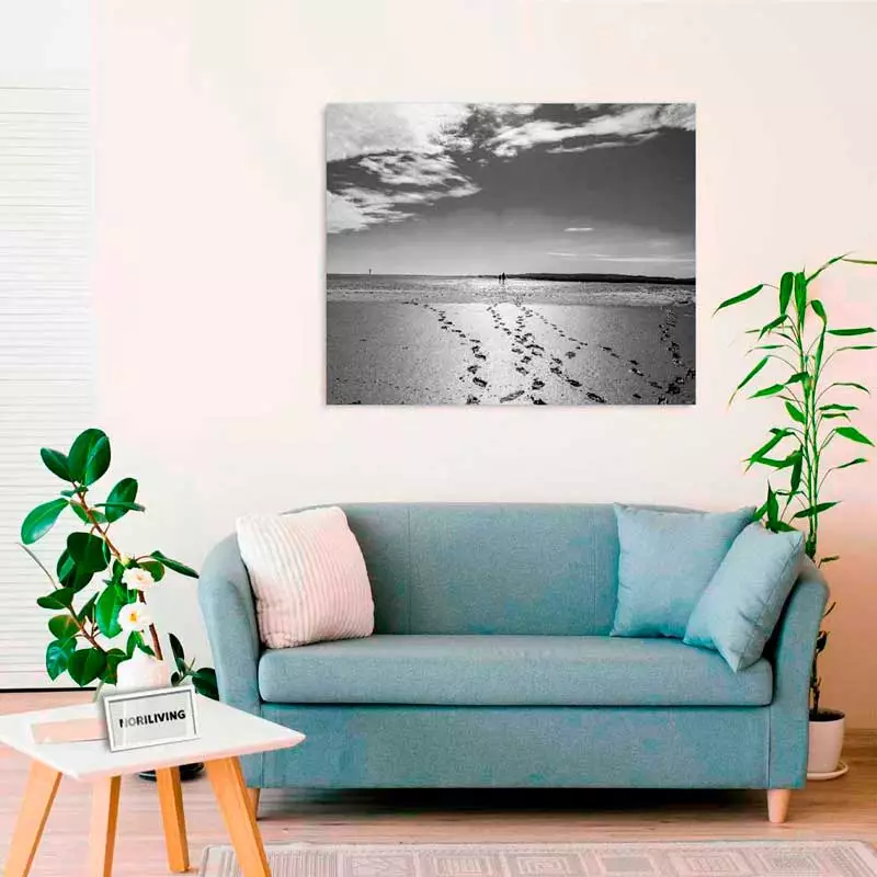 Wohnzimmer mit einem blauen Sofa, flankiert von Pflanzen, und einem großen Schwarz-Weiß-Bild an der Wand, das einen Strand mit Fußspuren zeigt.