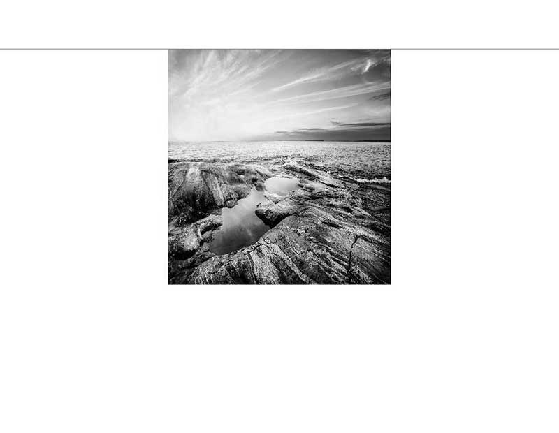 Schwarz-Weiß-Foto einer felsigen Küste mit Pfützen und einem weiten Meereshorizont