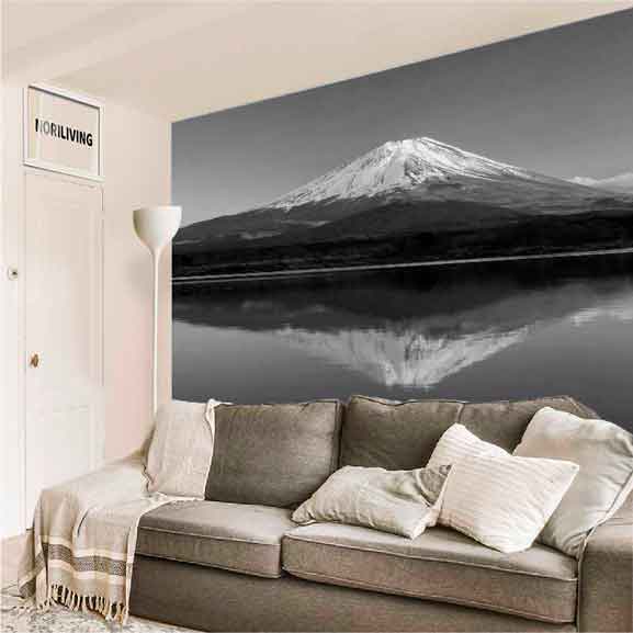 Gemütliches Wohnzimmer mit grauem Sofa und einer großflächigen Wandtapete, die einen schneebedeckten Berg und dessen Spiegelung im Wasser zeigt.