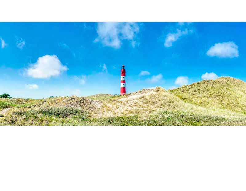 Ein roter Leuchtturm steht inmitten von Dünen unter einem strahlend blauen Himmel mit einigen Wolken.