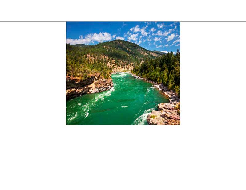 Panoramablick auf einen grünen Fluss, umgeben von bewaldeten Bergen und blauem Himmel mit einigen Wolken