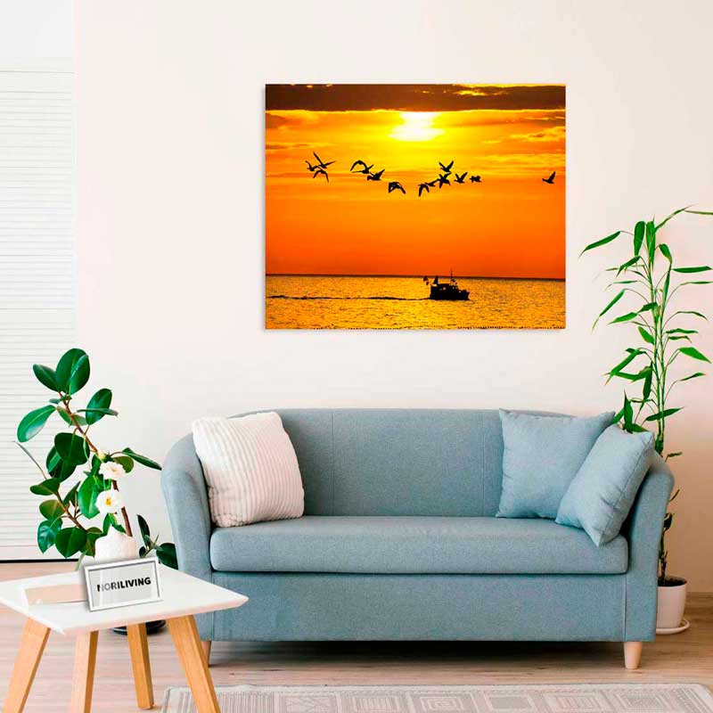 Modernes Wohnzimmer mit blauem Sofa, Topfpflanzen und Leinwandbild eines Sonnenuntergangs über dem Meer, mit fliegenden Möwen und einem Boot.