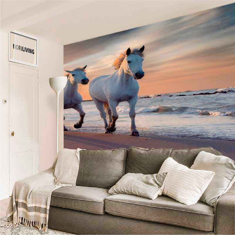 Stilvoll eingerichtetes Wohnzimmer mit grauem Sofa und großer Wandtapete, die zwei weiße Pferde am Strand bei Sonnenuntergang zeigt