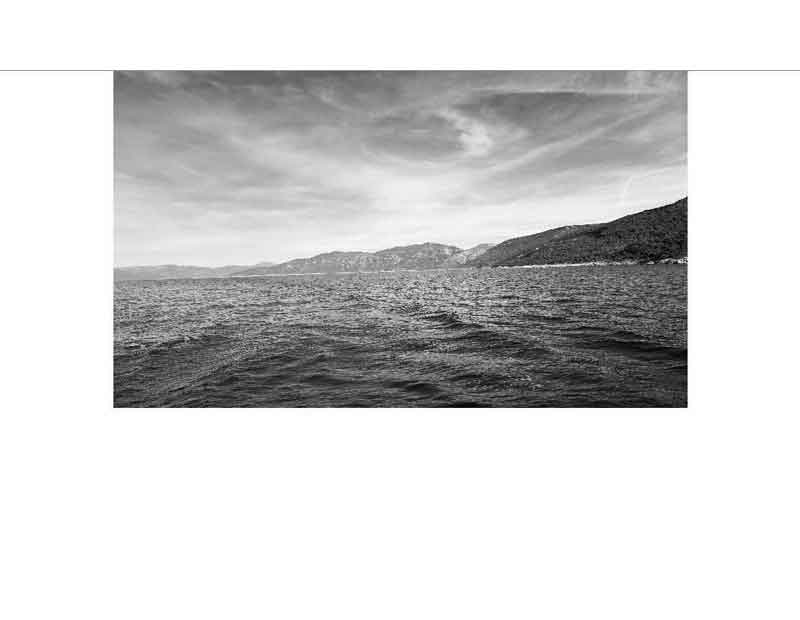 Ein ruhiger See in Schwarz-Weiß mit einer Bergkette im Hintergrund und bewölktem Himmel.