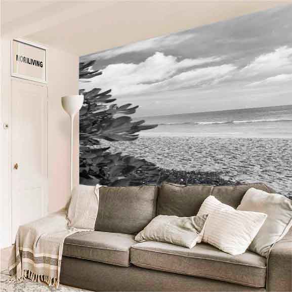 Modernes Wohnzimmer mit grauem Sofa, hellen Kissen und einer großen Fototapete eines Strandes in Schwarz-Weiß.