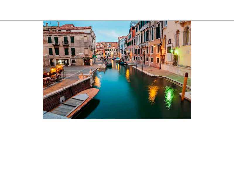 Ein ruhiger Kanal in Venedig bei Abenddämmerung mit beleuchteten historischen Gebäuden und Booten am Ufer.