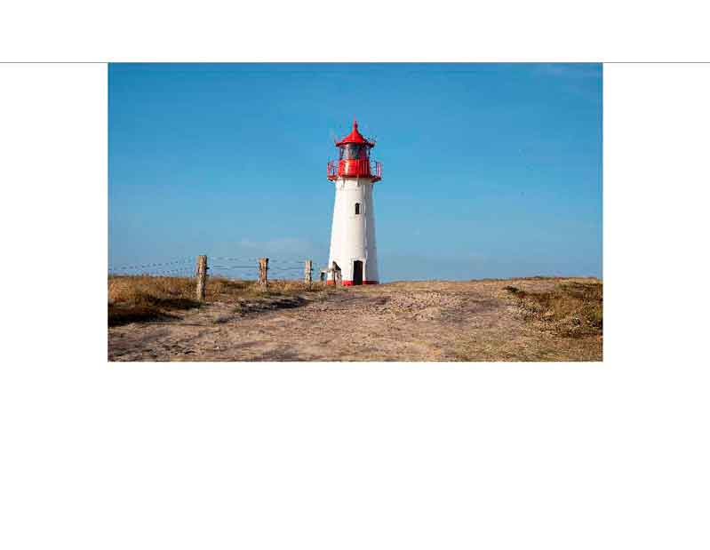 Ein weißer Leuchtturm mit roter Kuppel steht auf einer felsigen Klippe unter einem klaren blauen Himmel.
