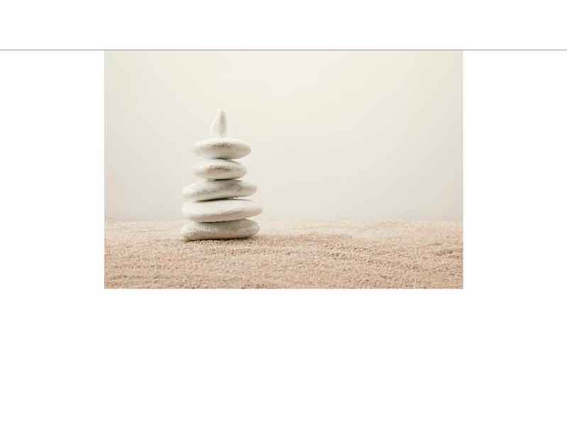 Eine kleine Pyramide aus weißen Steinen auf sandigem Untergrund, die Balance und Ruhe symbolisiert.