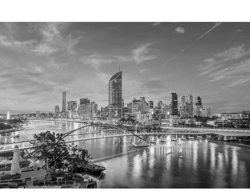 Schwarz-Weiß-Panoramablick auf eine moderne Stadtlandschaft bei Sonnenuntergang Schwarz-Weiß-Foto einer Stadt mit Fluss und Brücke im Vordergrund, beleuchtete Wolkenkratzer im Hintergrund