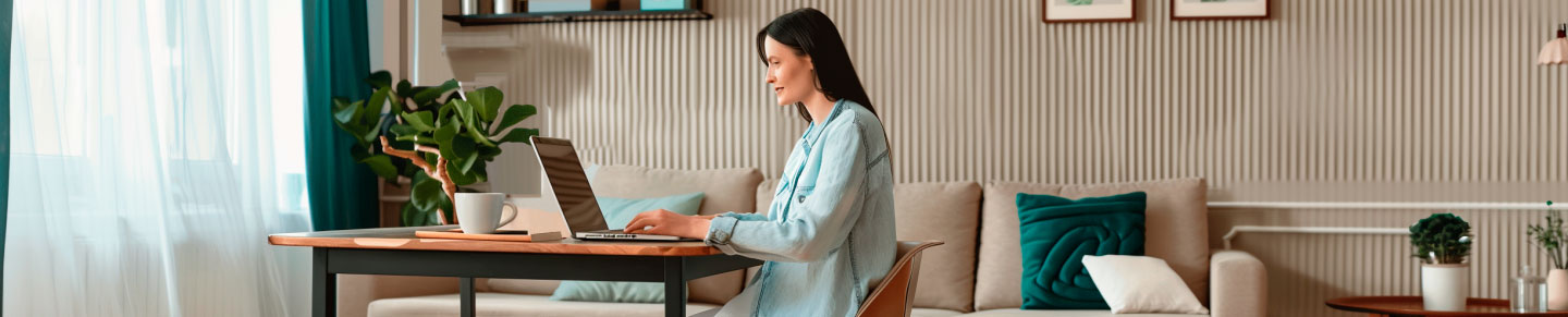 Eine Frau arbeitet an einem Laptop im gemütlich eingerichteten Wohnzimmer mit Pflanzen und moderner Dekoration.