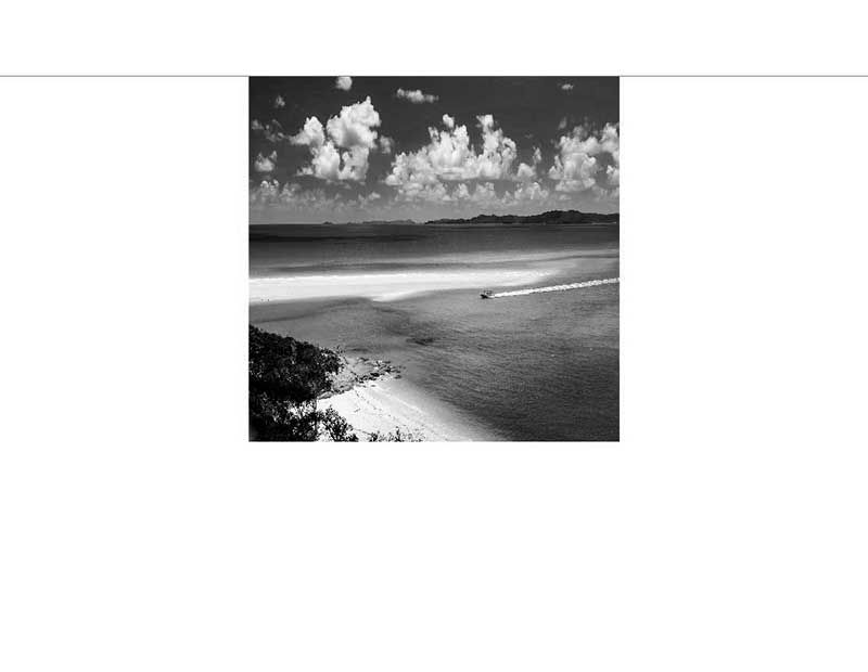 Schwarzweißfoto eines ruhigen Strandes mit Boot auf dem Wasserhorizont Ein sandiger Strand erstreckt sich unter einem Himmel voller Wolken mit einem Boot, das eine Spur auf dem Wasser hinterlässt