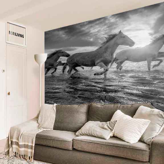 Ein Wohnzimmer zeigt eine schwarz-weiße Tapete mit galoppierenden Pferden und ein graues Sofa mit Kissen vor der Tapete.