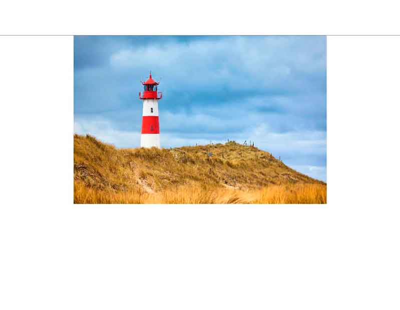 Ein rot-weißer Leuchtturm steht auf einer Düne, umgeben von Gras, unter einem bewölkten Himmel.