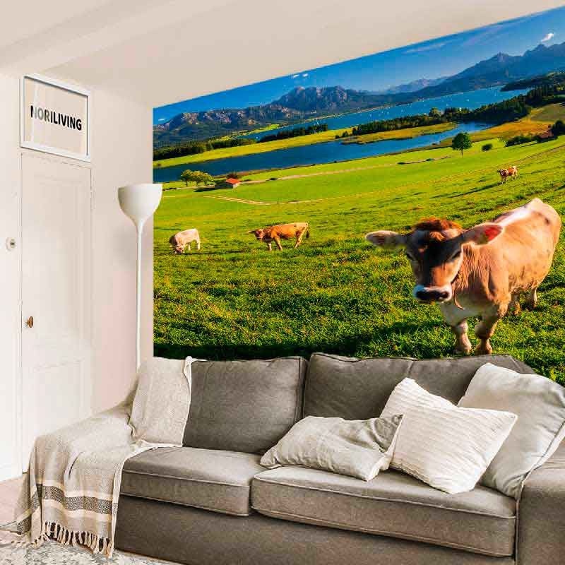 Gemütliches Wohnzimmer mit grauem Sofa und eindrucksvoller Fototapete von grünen Almwiesen und Kühen im Hintergrund