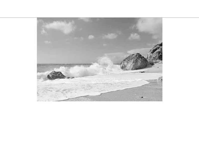Schwarzweißaufnahme eines Strandes mit Wellen und Felsen