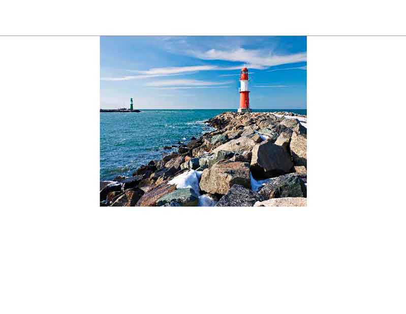 Ein roter Leuchtturm steht auf einer felsigen Küste am Meer, unter einem blauen Himmel mit wenigen Wolken.