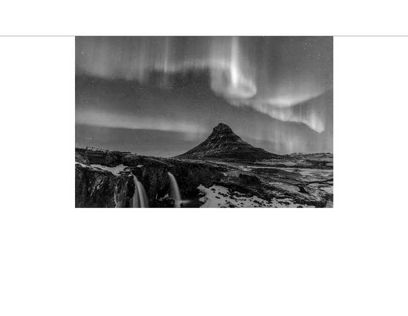 Schwarzweißfoto des Kirkjufell, einem Berg in Island, umrahmt von Nordlichtern und winterlicher Landschaft
