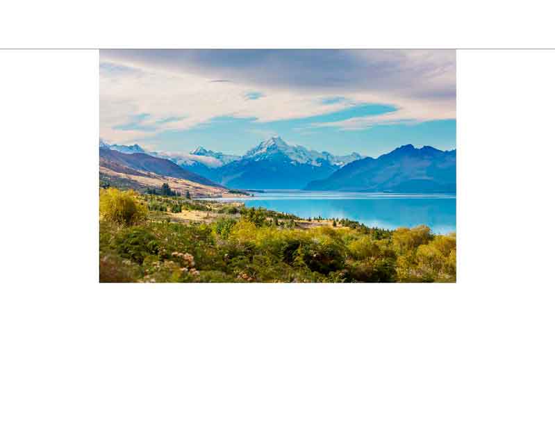 Panoramablick auf einen See vor schneebedeckten Bergen mit üppiger Vegetation im Vordergrund