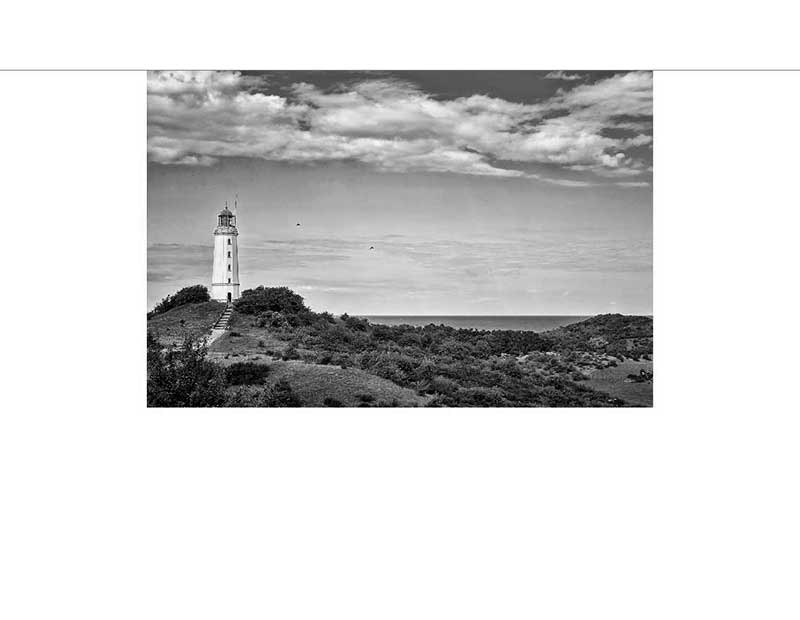 Ein Leuchtturm steht auf einem Hügel mit Blick auf die Küstenlandschaft, umgeben von Wolken.