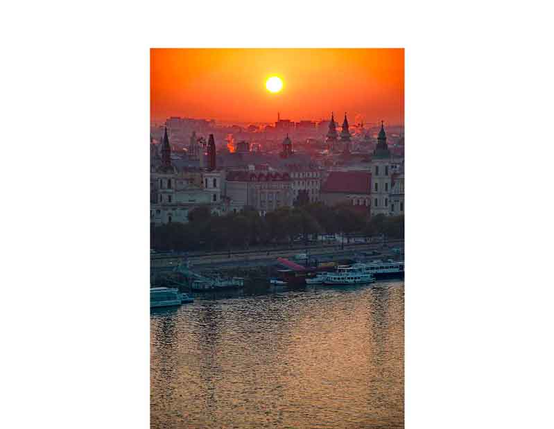 Sonnenuntergang über der Stadt mit Fluss im Vordergrund Ein wunderschöner Sonnenuntergang hinter einer Stadtansicht, während ein Fluss im Vordergrund fließt
