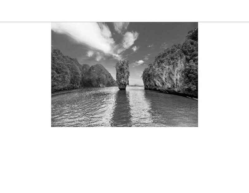 Schwarz-Weiß-Fotografie einer markanten Felsformation im Wasser Eine beeindruckende Felsformation erhebt sich aus dem Wasser inmitten einer natürlichen Umgebung, Schwarz-Weiß-Foto.