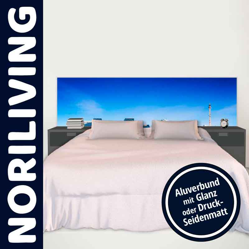 Bett mit weißer Bettwäsche und Aluverbund-Kopfteil mit blauem Himmel-Motiv in Glanzoptik, umgeben von Nachttischen mit Büchern und Uhr.