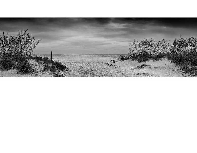 Schwarz-Weiß-Foto eines Sandstrandes mit Dünen und bewölktem Himmel Ruhige Strandlandschaft in Schwarz-Weiß mit Dünen und Wolken am Himmel