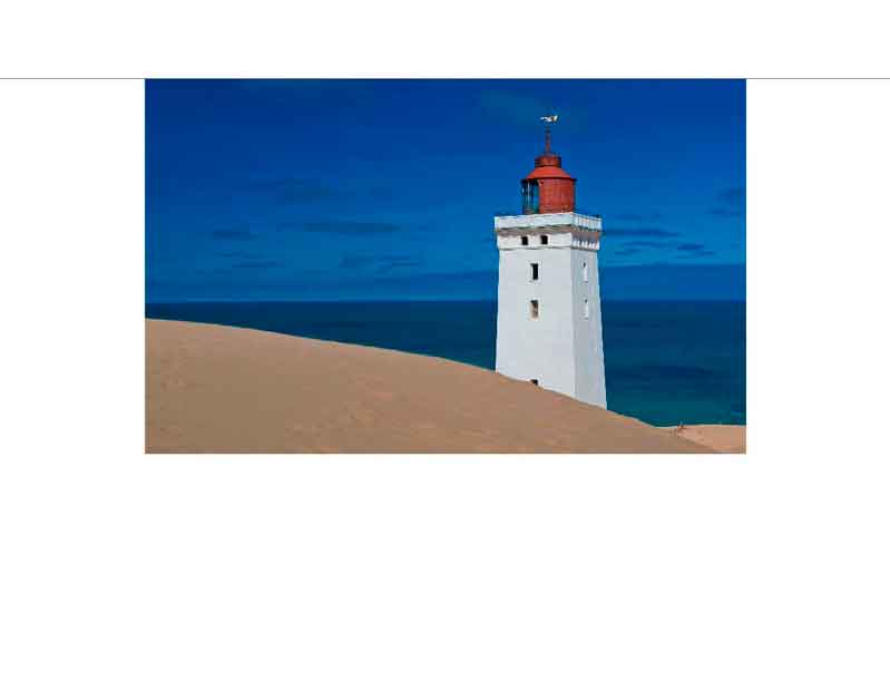 Ein weißer Leuchtturm mit rotem Dach steht an einem sonnigen Sandstrand mit blauem Himmel und Meer im Hintergrund.