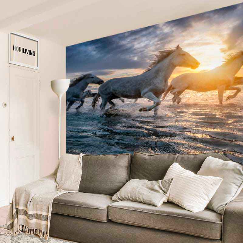 Wanddekoration mit Pferden am Strand, beleuchtet von der Abendsonne, hinter einem grauen Sofa im modernen Wohnbereich