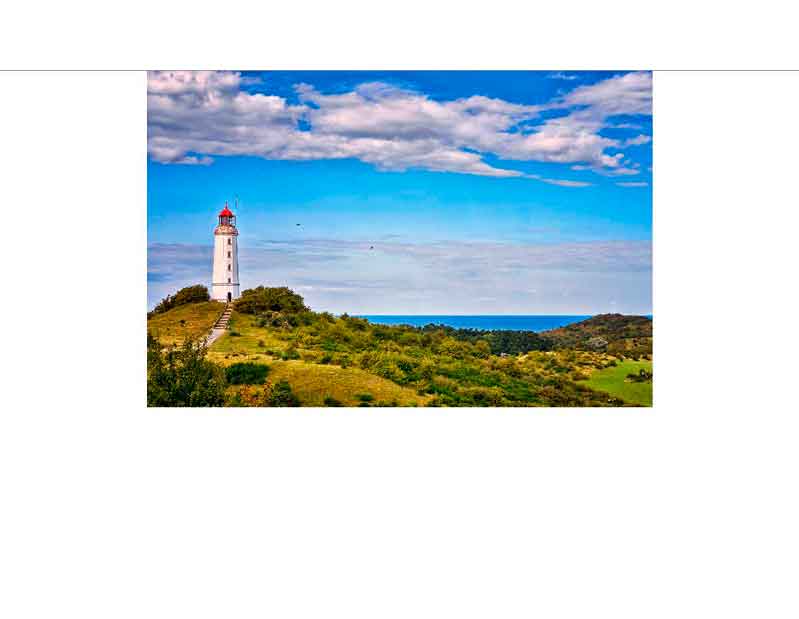 Ein weißer Leuchtturm mit roter Kuppel erhebt sich auf einem grünen Hügel vor einem klaren blauen Himmel und Meer im Hintergrund.