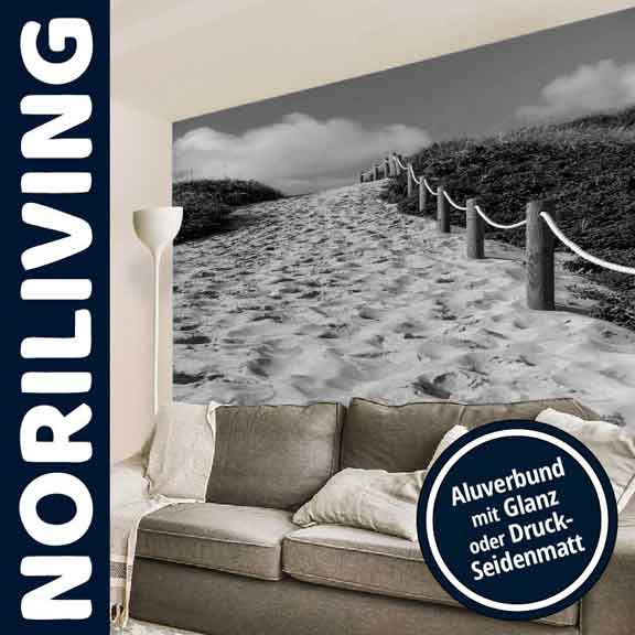 Ein Wohnzimmer mit einem großen Wandbild zeigt einen Strandweg mit Dünen und Seilen aus Perspektive eines Sofas. Beschriftung: Aluverbund mit Glanz oder Druck-Seidenmatt.