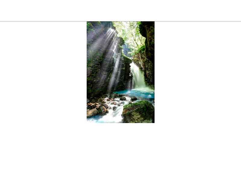 Ein idyllischer Wasserfall, der durch eine üppig bewachsene Felsenschlucht fließt, beleuchtet von sanften Sonnenstrahlen.