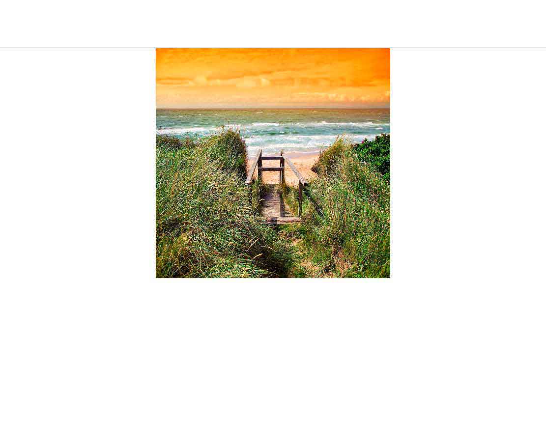 Ein schmaler Holzweg führt durch Dünen zum Strand, der von einem orangefarbenen Himmel bei Sonnenuntergang beleuchtet wird.