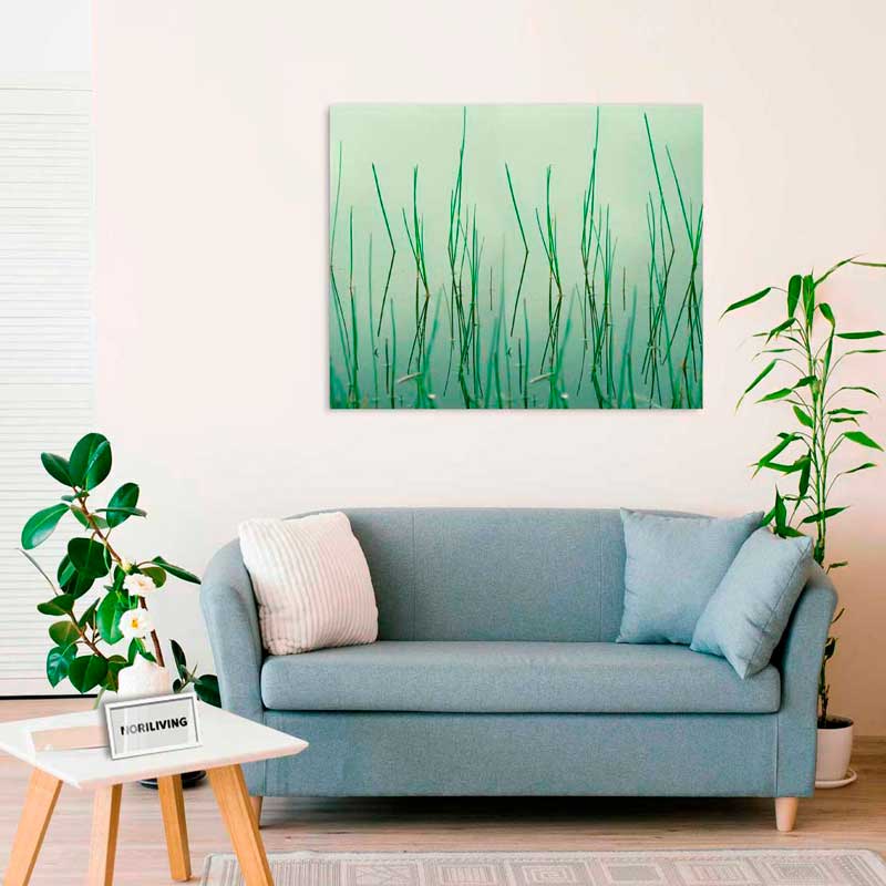 Moderne Wohnzimmerdekoration mit blauem Sofa und Wandbild mit Grasmotiv Innenraum mit blauem Sofa, beige Kissen und grünem Wandbild über Pflanzen