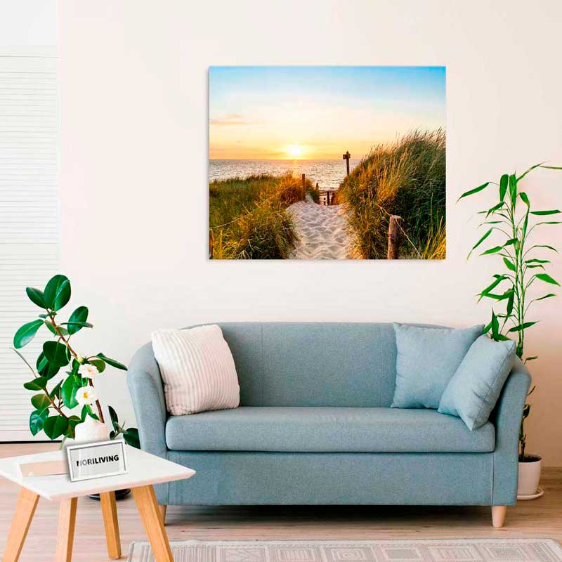 Ein modernes Wohnzimmer mit einem hellblauen Sofa und einem großen Wandbild, das eine Strandlandschaft im Sonnenuntergang zeigt.