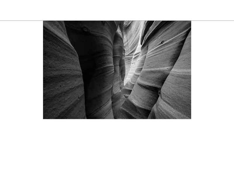 Schwarzweißfoto eines engen Schluchtabschnitts mit wellenförmigen Felswänden eines Slot-Canyons