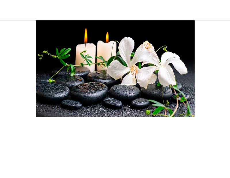 Zwei brennende Kerzen, weiße Blüten und glatte schwarze Steine in einem spa-ähnlichen Setting zur Entspannung