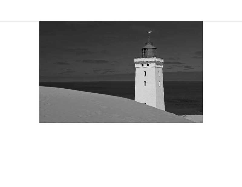 Ein Leuchtturm steht auf einem Hügel mit Meer im Hintergrund, in Schwarz-Weiß.