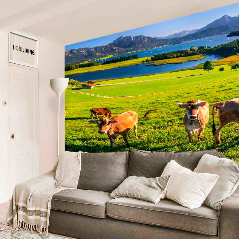 Wandbild mit Kühen und Bergblick im Wohnzimmer Gemütliches Wohnzimmer mit großem Wandbild, das eine grüne Wiese mit Kühen und einem malerischen Berg- und Seepanorama zeigt.