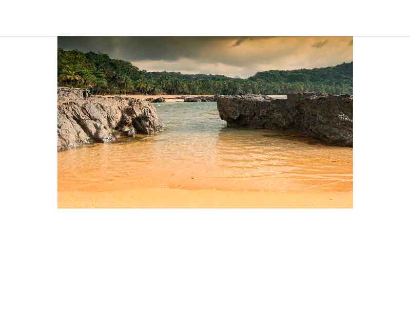 Strandlandschaft mit ruhigem Wasser, felsigen Ufern und tropischem Wald im Hintergrund