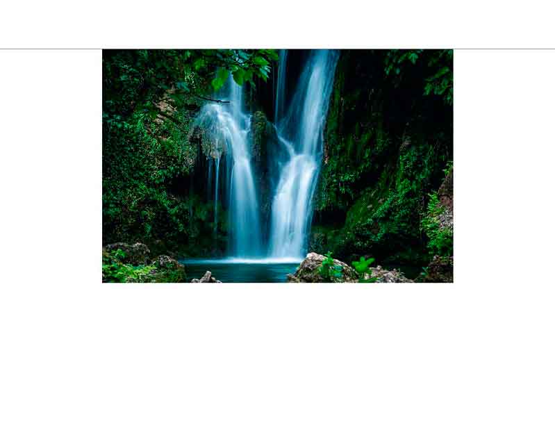 Ein beeindruckender Wasserfall, umgeben von grüner Vegetation und Felsen, fließt in einen klaren Pool darunter.