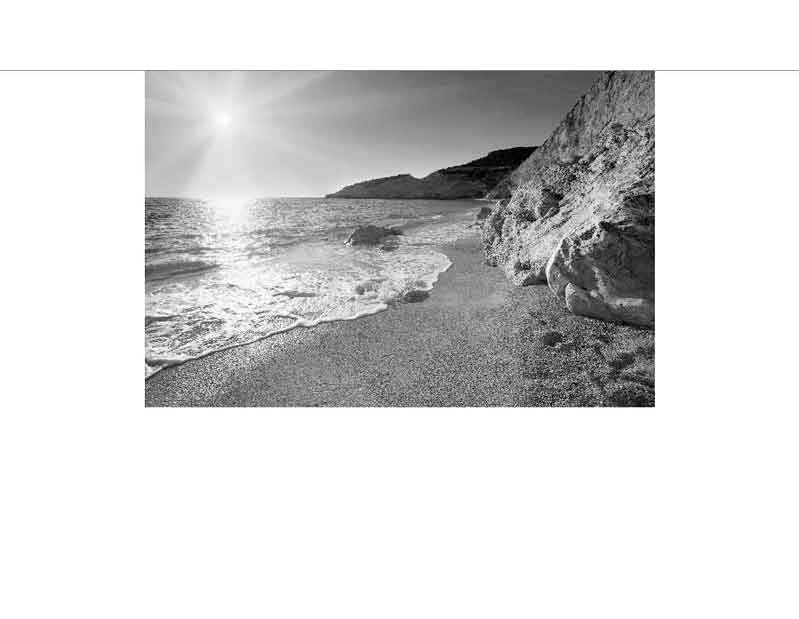 Sonnenuntergang am felsigen Strand Schwarzweißfoto eines sonnigen Tages an einem felsigen Strand mit sanften Wellen