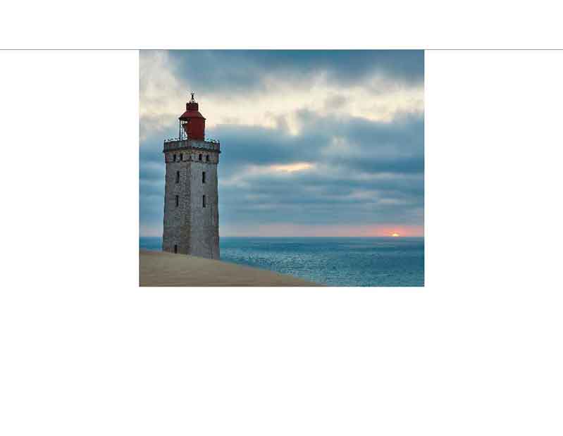 Ein Leuchtturm steht auf einer Düne am Meer, während die Sonne am Horizont untergeht.