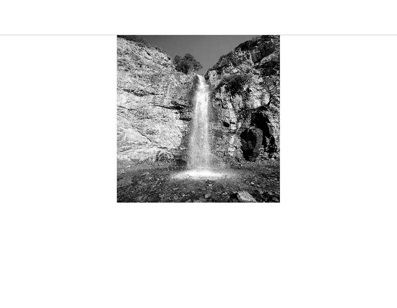 Ein Wasserfall stürzt in dramatischer Schwarzweiß-Darstellung über Felsen hinab.