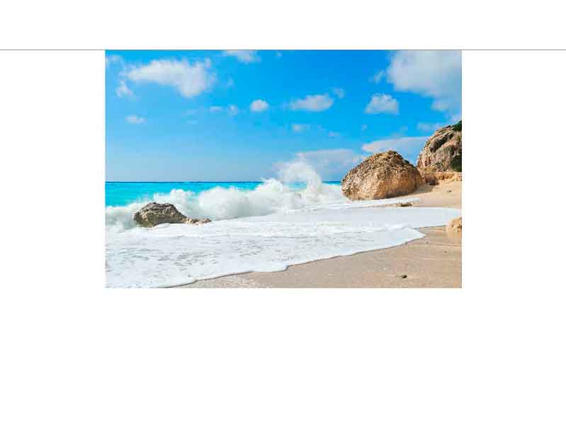 Ein unberührter Sandstrand mit klarem blauem Wasser und Felsen im Hintergrund, über denen sich weiße Wolken befinden