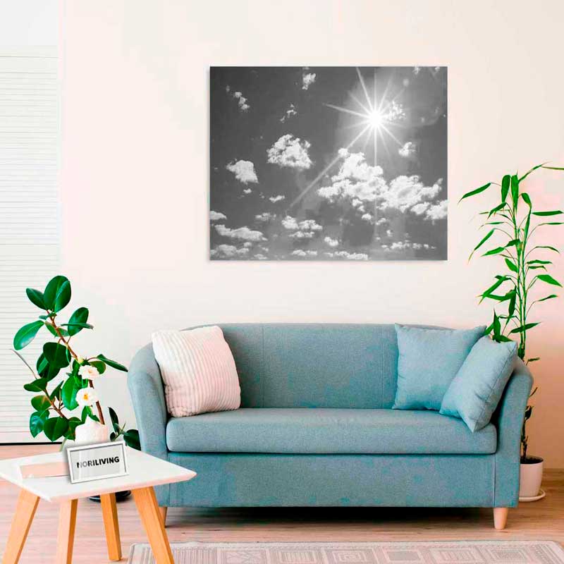 Ein Wohnzimmer mit blauem Sofa, Pflanzen und einem monochromen Kunstwerk mit Wolken und Sonne an der Wand.
