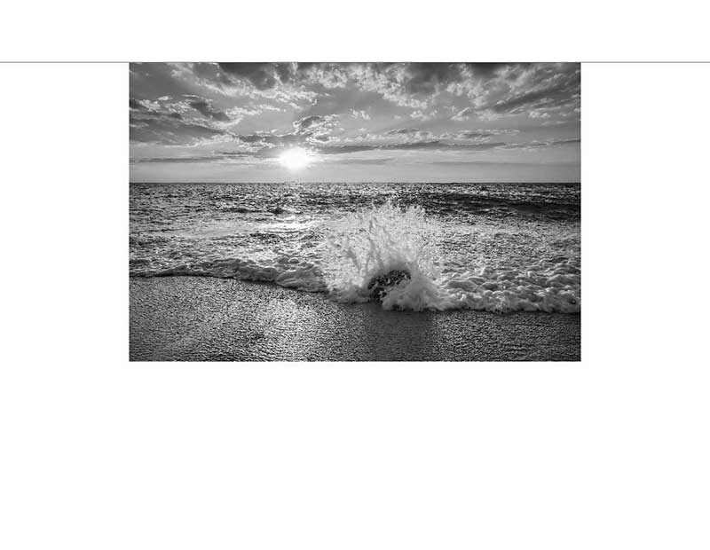 Schwarz-Weiß-Fotografie eines Wellenbruchs bei Sonnenuntergang Dramatischer Wellenbruch an einem Strand bei Sonnenuntergang, in Schwarz-Weiß gehalten