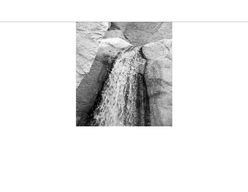 Ein kleiner Wasserfall fließt über Felsen in einer natürlichen Umgebung. Schwarz-Weiß-Fotografie.