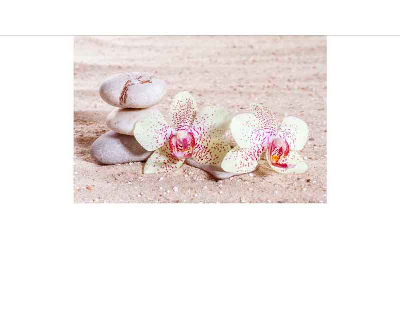 Drei runde Steine gestapelt neben zwei blühenden Orchideen auf einem Sandhintergrund